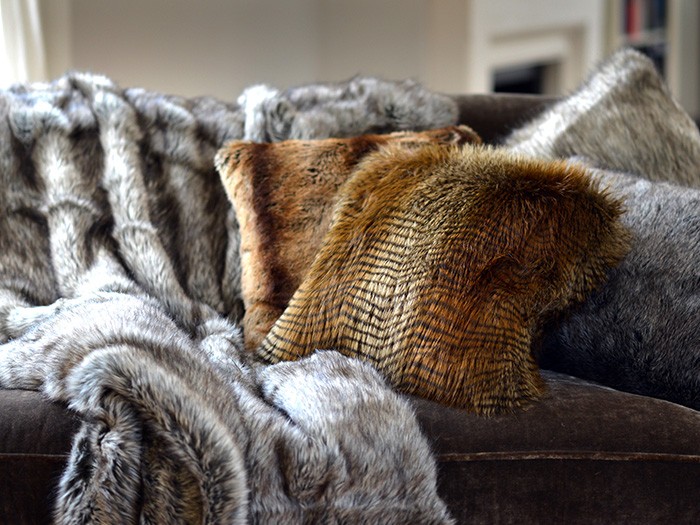 Couverture en fausse fourrure et coussins d’appoint en fausse fourrure posés sur un canapé de couleur sombre. 