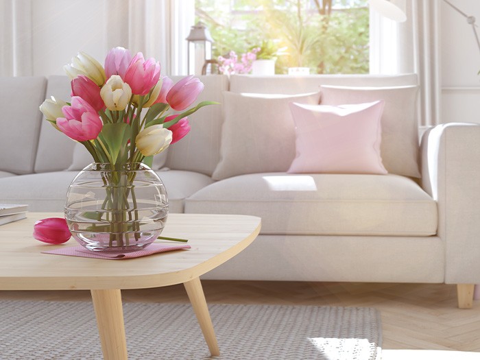 Salon avec des meubles de couleur neutre décorés de coussins décoratifs rose vif et de fleurs.