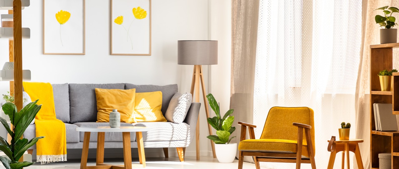 Salon lumineux, éclairé par la lumière naturelle, avec un canapé gris, des coussins décoratifs jaunes, des couvertures et une chaise décorative.