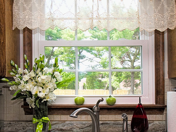 Fenêtre de cuisine au-dessus de l’évier avec une cantonnière en tissu blanc transparent.
